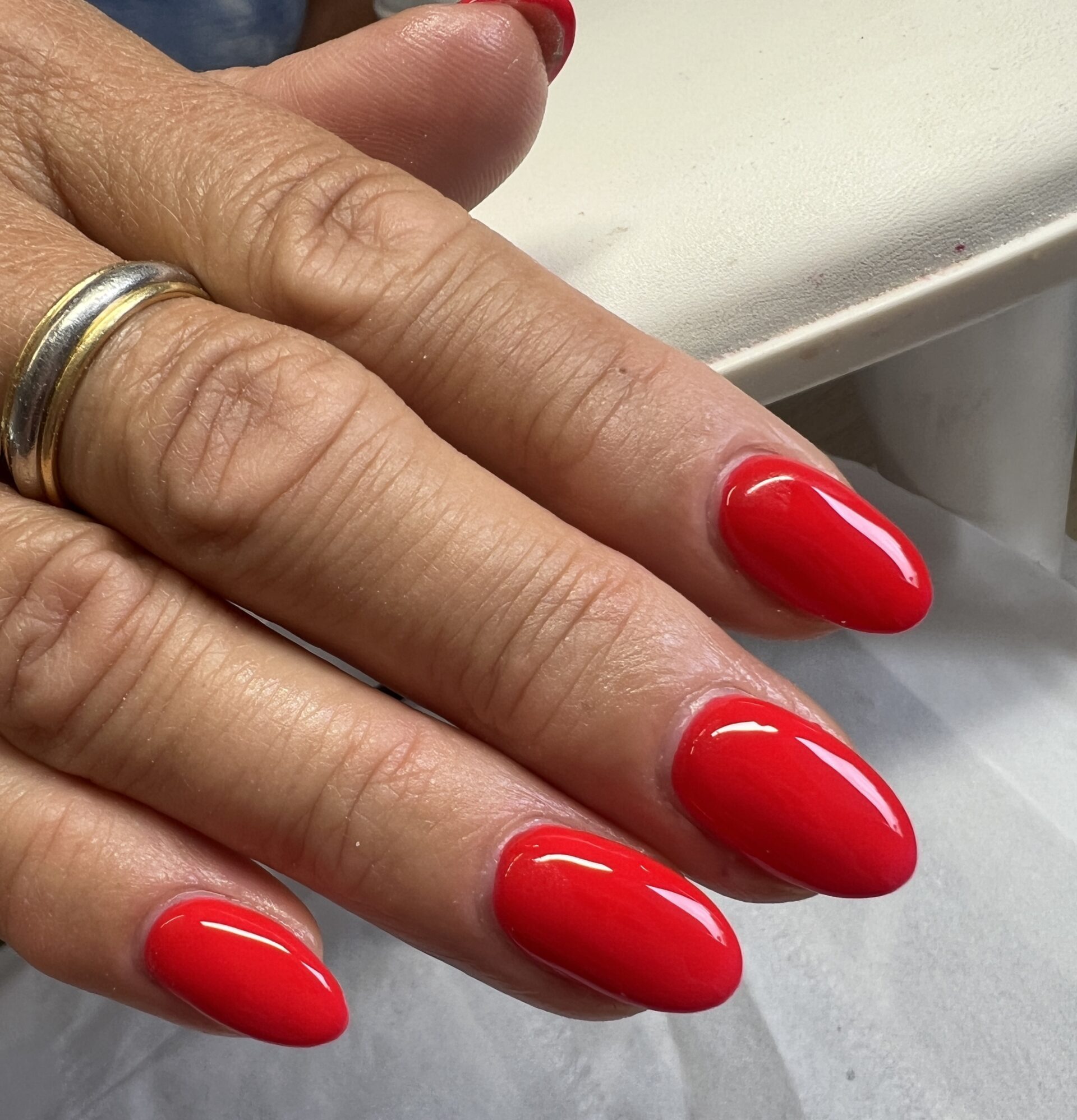 Completed BIAB nail service showing vibrant, high-gloss red polished applied to oval-shaped nails.